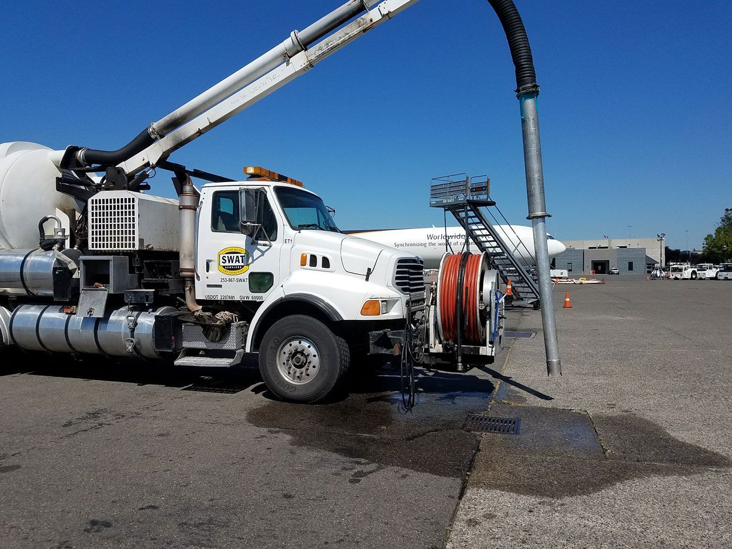 A white truck with a hose attached to it is parked in a parking lot.