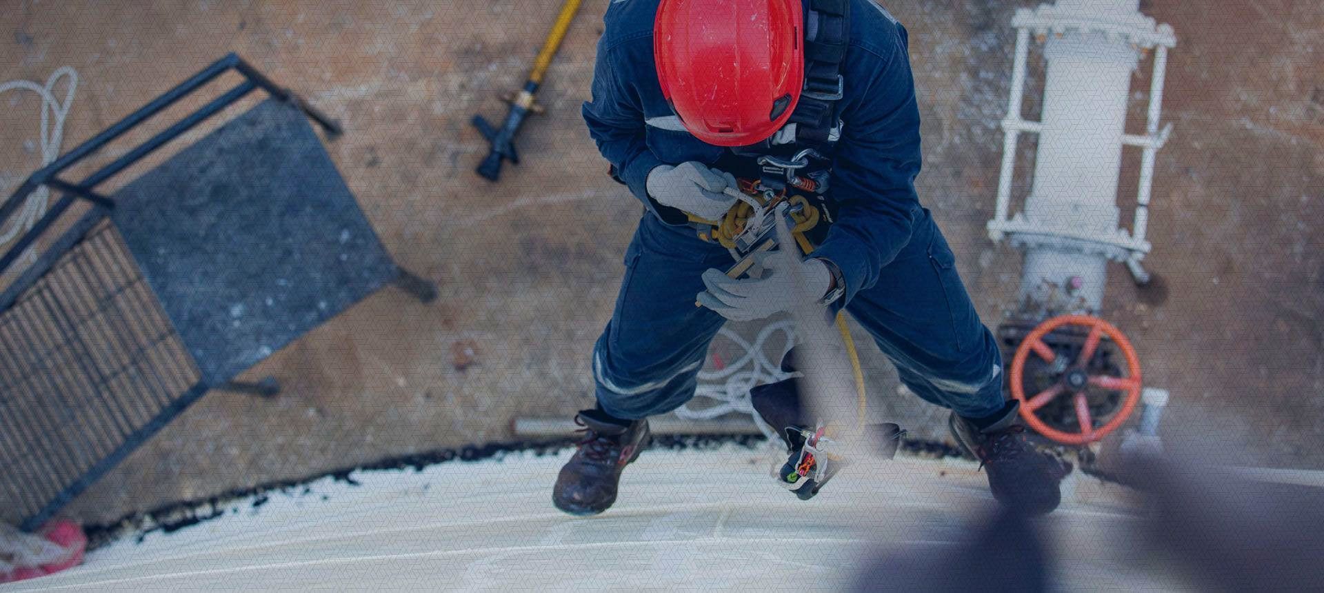 A man wearing a red hard hat is standing on top of a building.