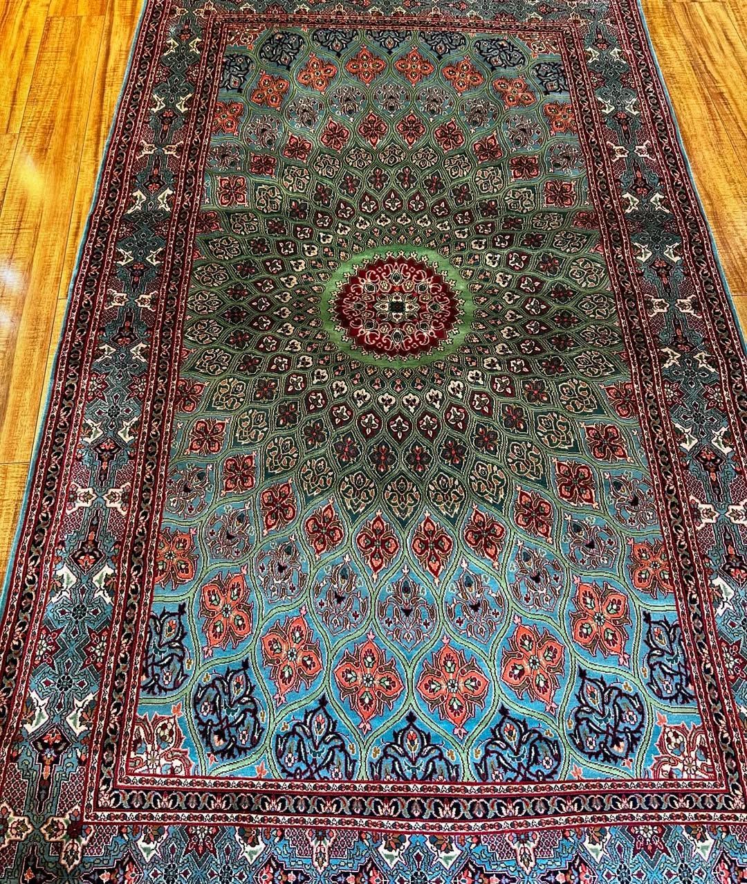 Oriental rug with a central medallion in green, blue, and red colors on a wooden floor.