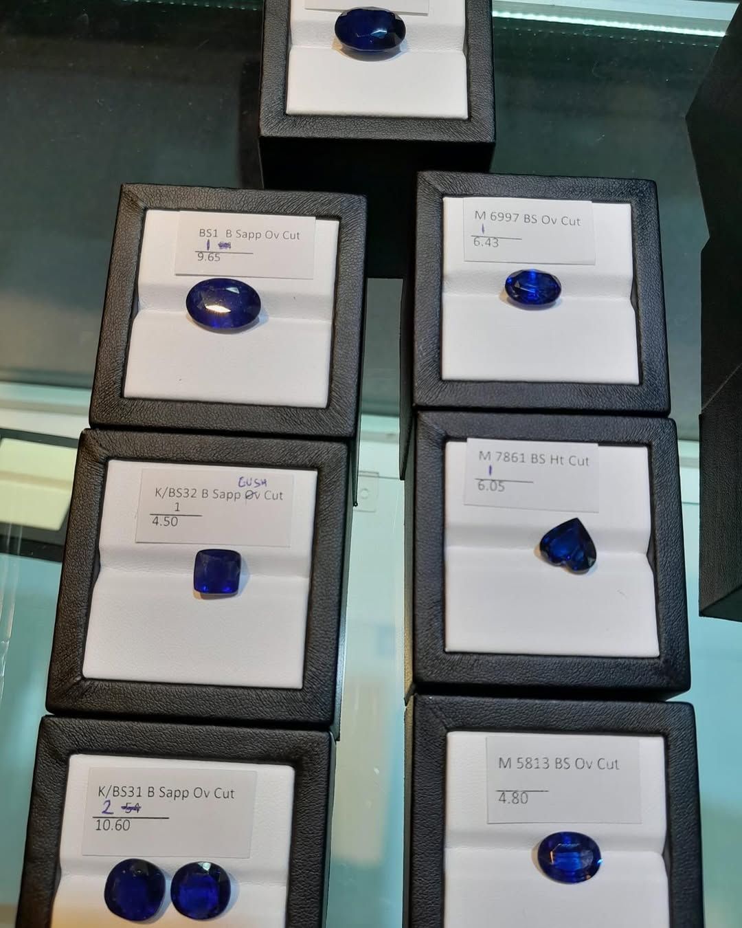 Sapphires in black display boxes with white inserts. Various shapes and sizes, deep blue color.