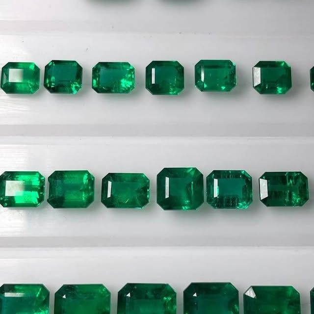 Rows of emerald green rectangular gemstones displayed on a white surface.