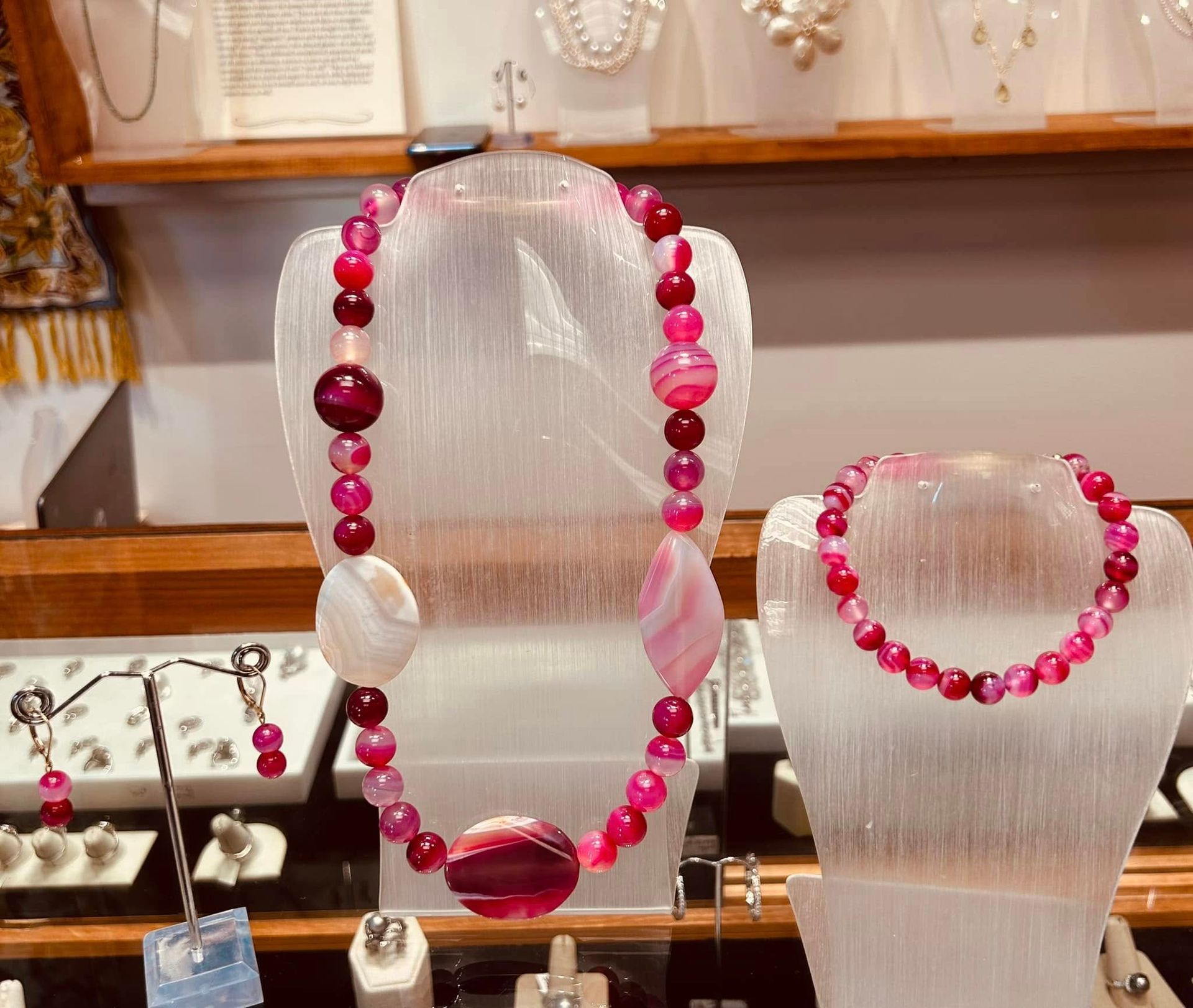 Pink beaded necklace and bracelet displayed on clear stands, along with matching earrings.