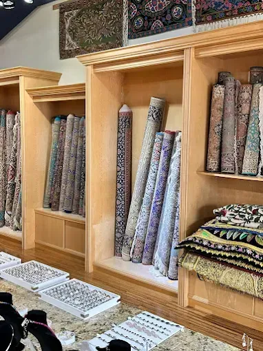 Inside a rug store, rolled and folded rugs displayed in wooden shelving.