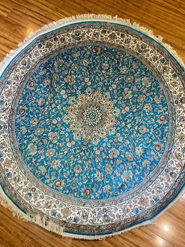 Round turquoise rug with floral pattern and fringe on wooden floor.