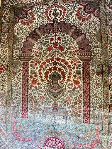 Detailed, ornate rug with floral and arch designs in red, green, and beige.