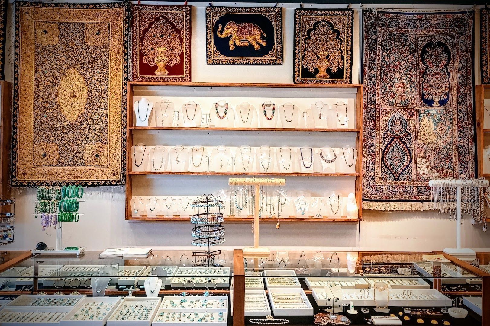 Jewelry store display with necklaces on shelves, glass counters, and ornate tapestries.