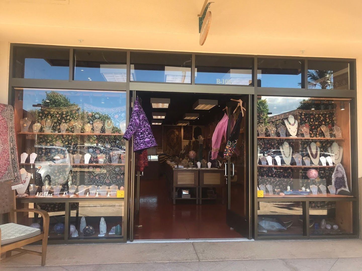 Exterior view of a jewelry store with glass windows showcasing necklaces and displays. Open doorway leads inside, red floor.