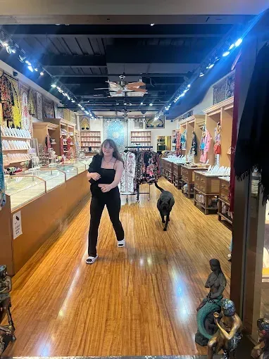 Woman and dog walk inside a store with wooden floors, displays of jewelry, and merchandise.