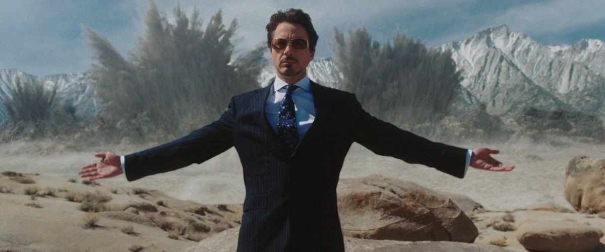 tony stark standing in front of mountains that are being blown up