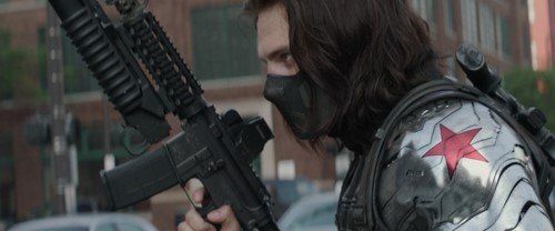 the winter soldier holding a rifle walking down a street