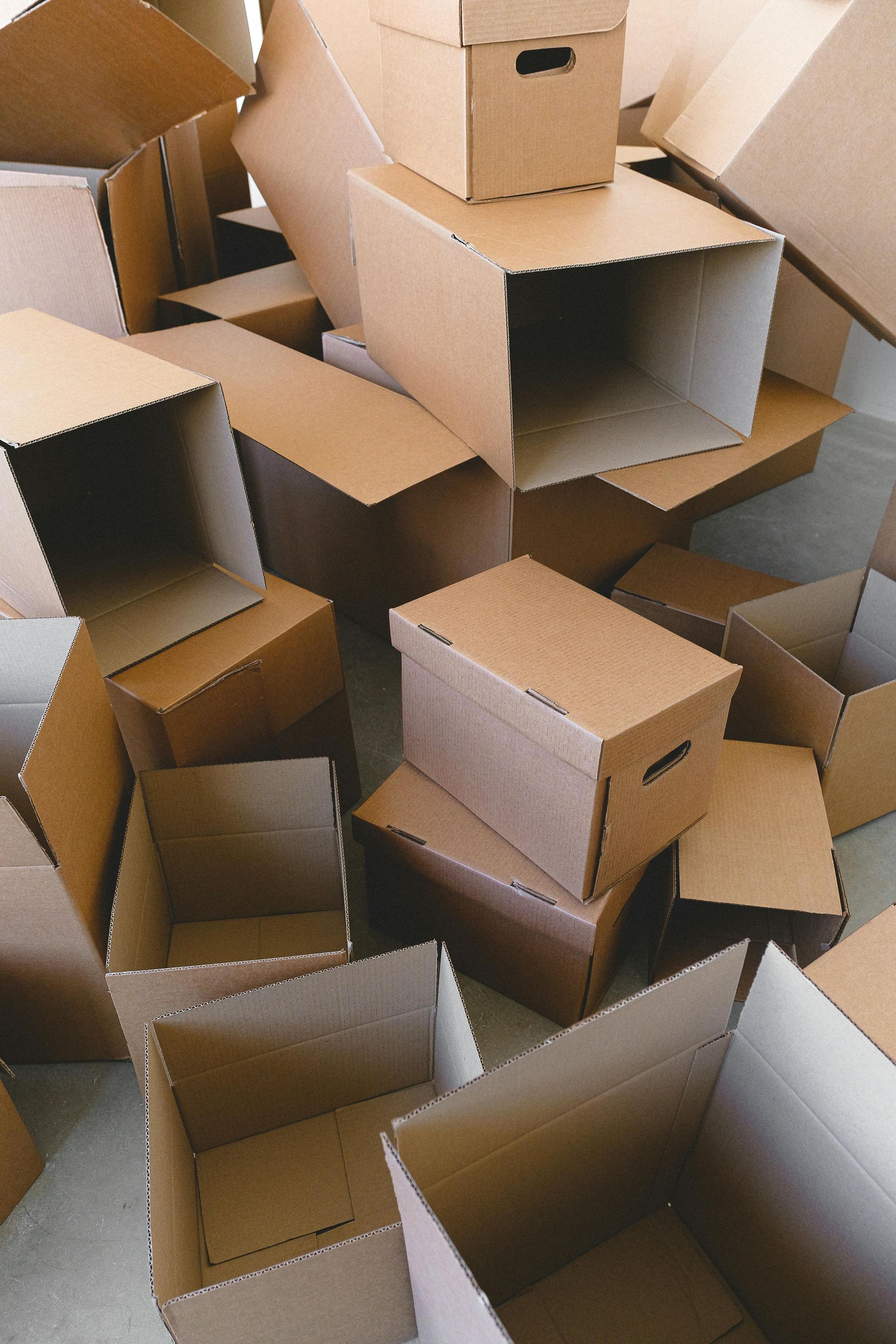 Pile of open and closed brown cardboard boxes, likely for moving or storage, on a floor.