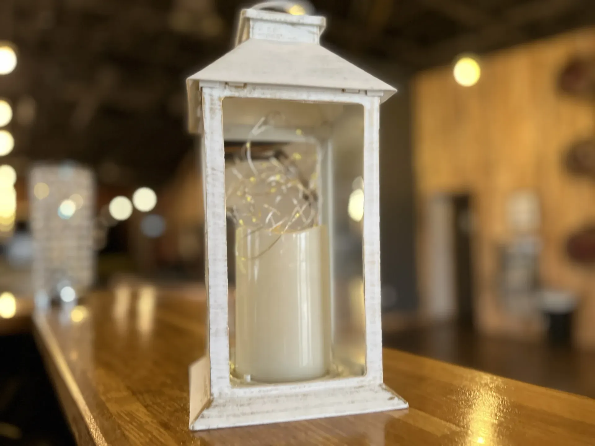 A white lantern with a candle inside of it is sitting on a wooden table.