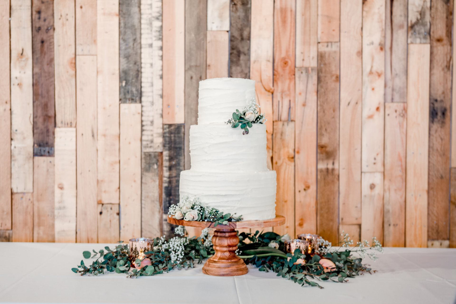 A wedding cake is sitting on a table in front of a wooden wall.