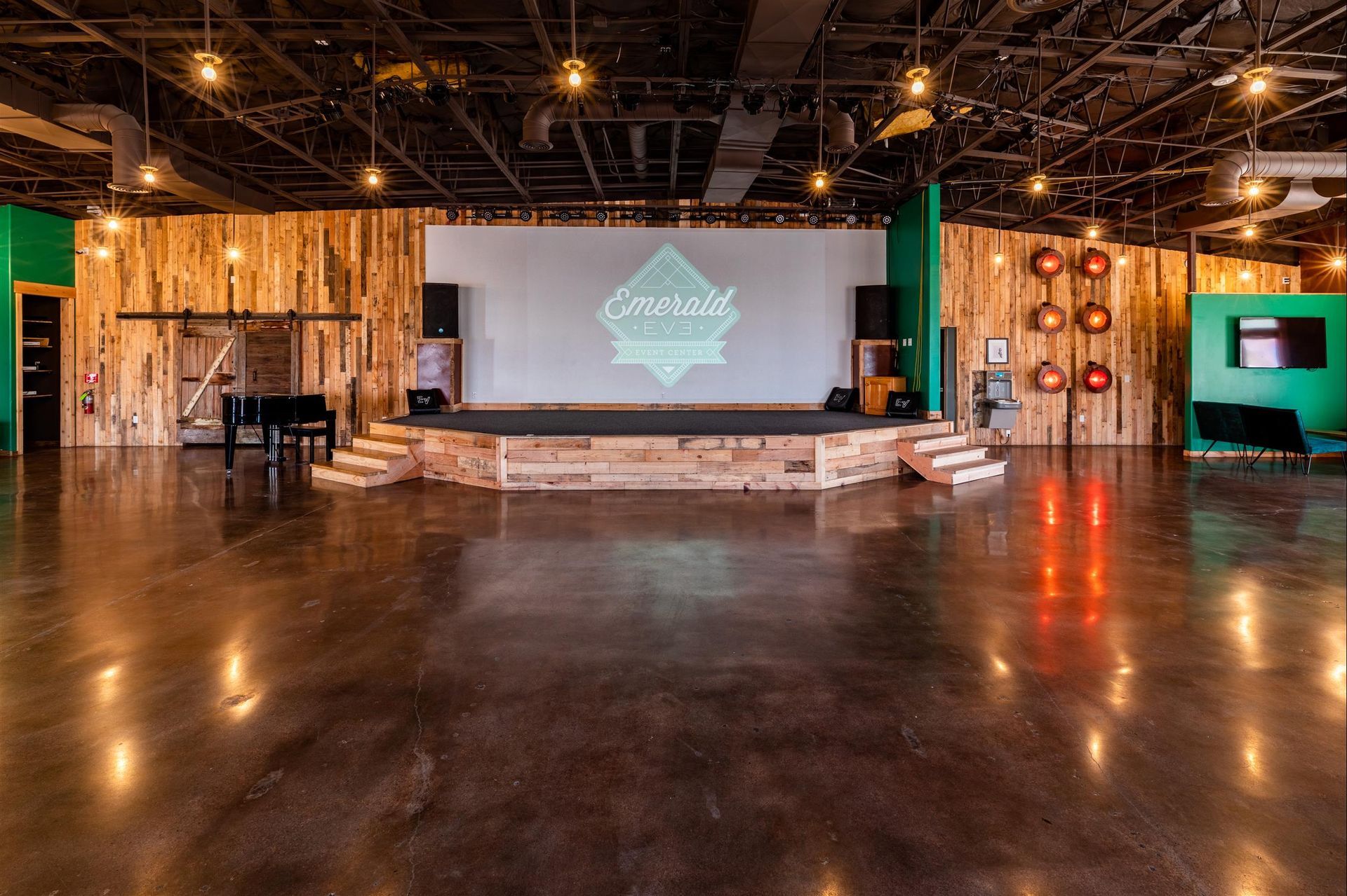 A large empty room with a stage and a projector screen.