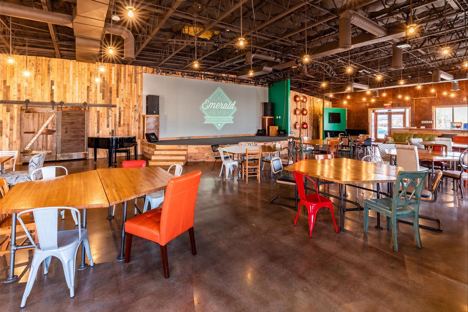 A large room with tables and chairs and a large screen on the wall.