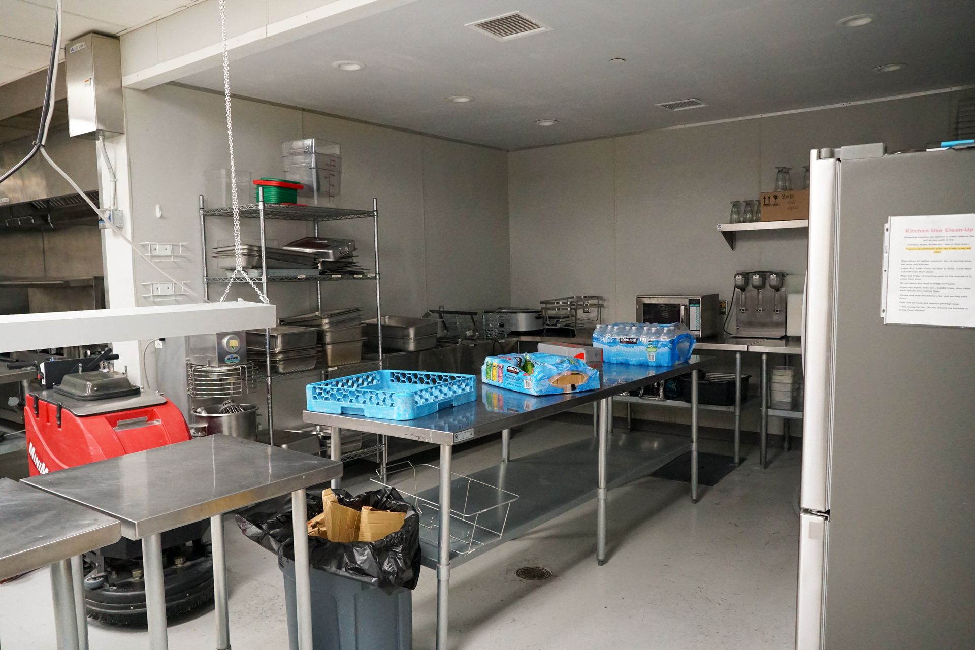 Commercial kitchen with stainless steel counters and shelves, blue crates, and appliances.