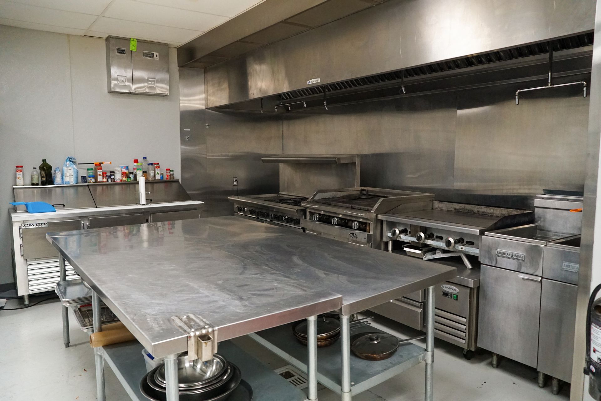 Commercial kitchen with stainless steel appliances, prep tables, and ventilation hood.