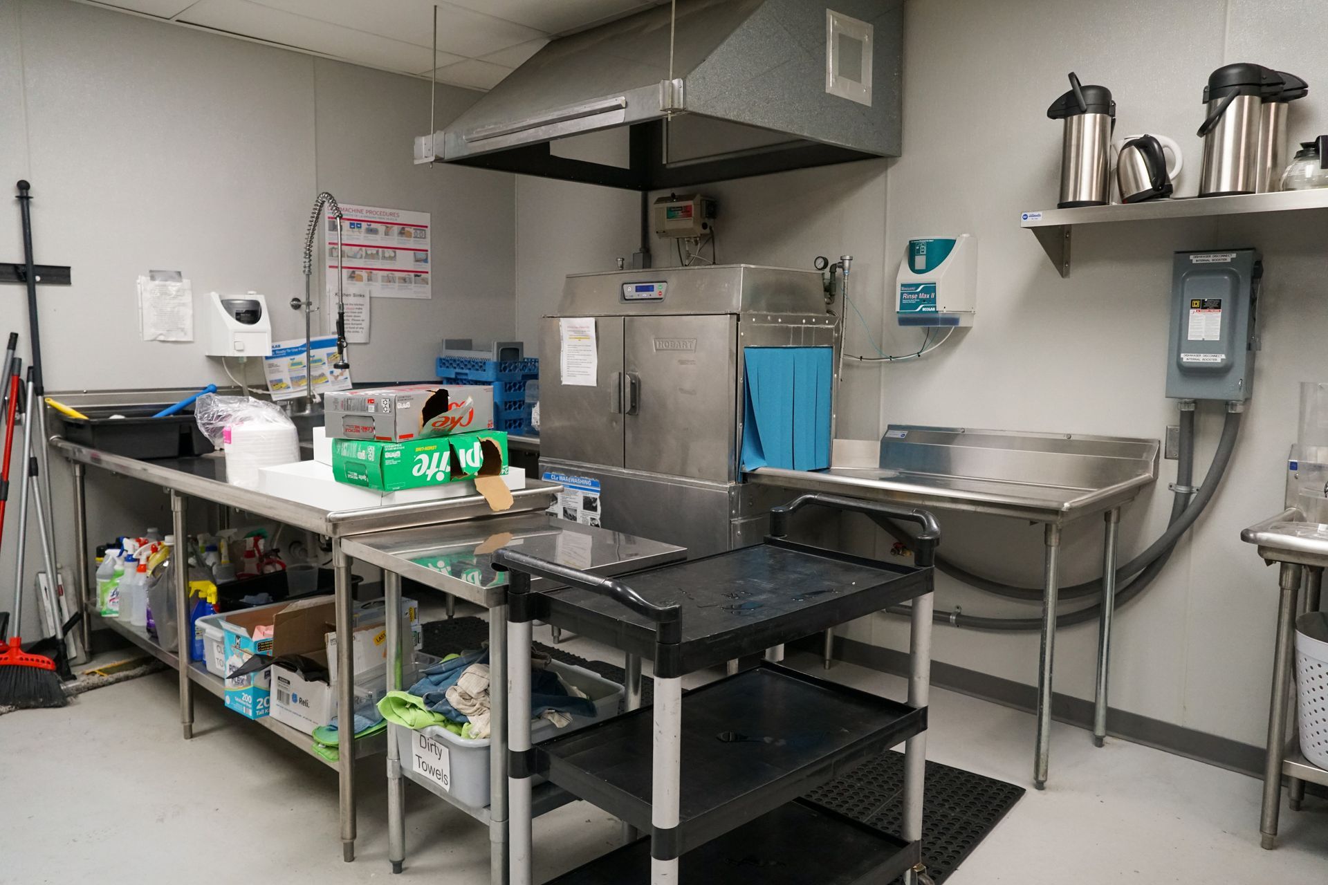 Commercial kitchen with stainless steel surfaces, dishwasher, and food prep area.