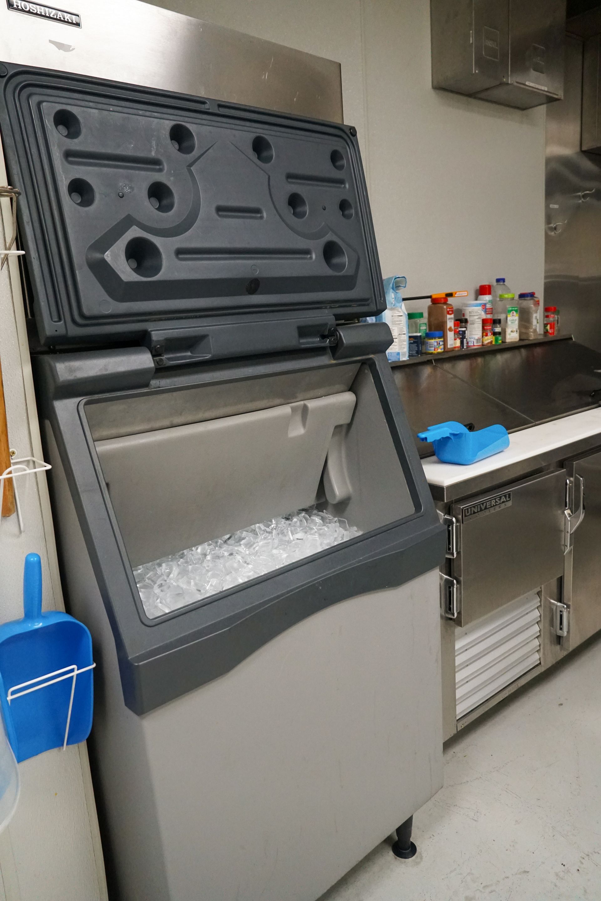 A commercial ice machine with an open lid, filled with ice in a kitchen.