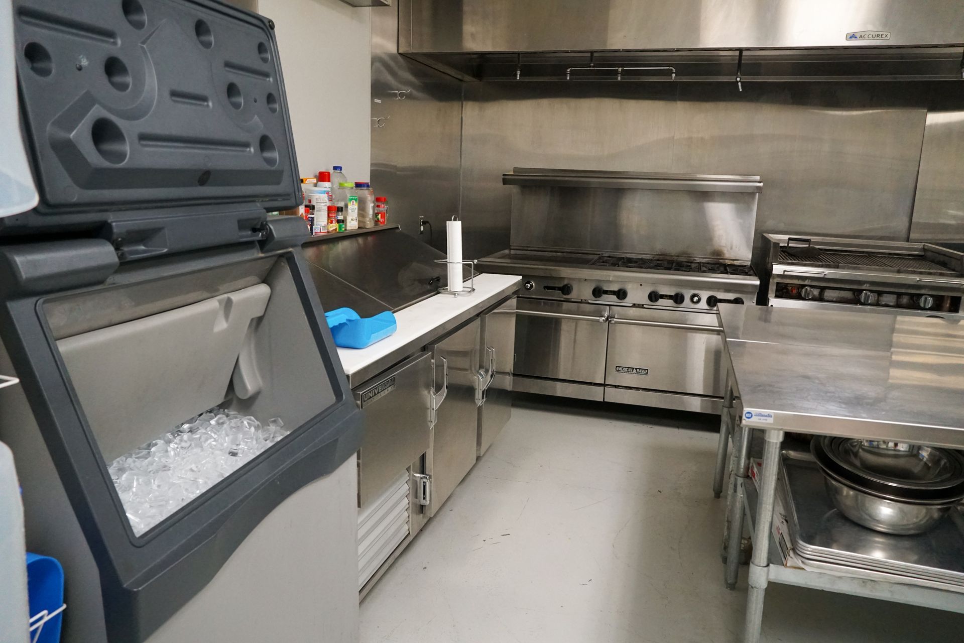 Commercial kitchen with ice machine, stainless steel appliances, and prep table.