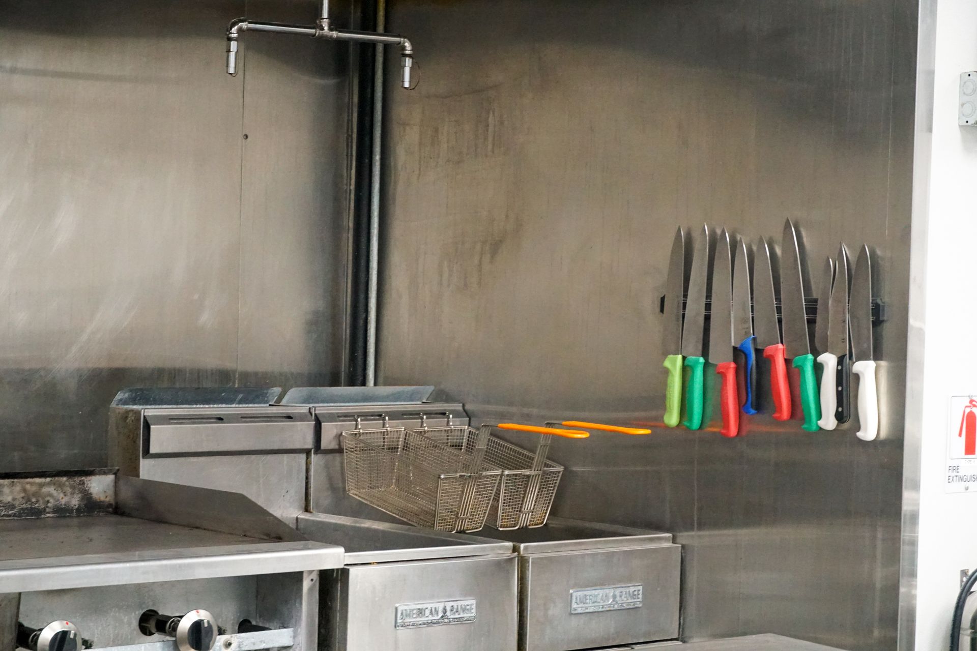 Stainless steel commercial kitchen with fry station and knives with colorful handles hanging.