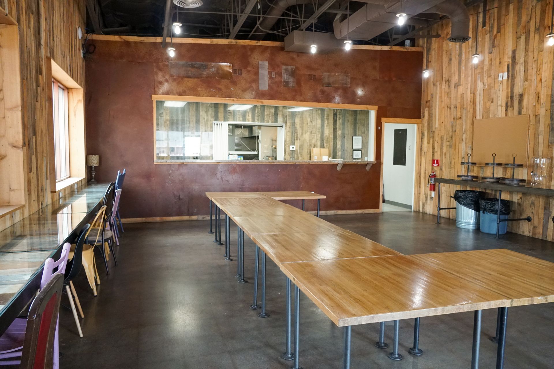 A rustic event space with a long wooden table, exposed wood walls, and a kitchen view.
