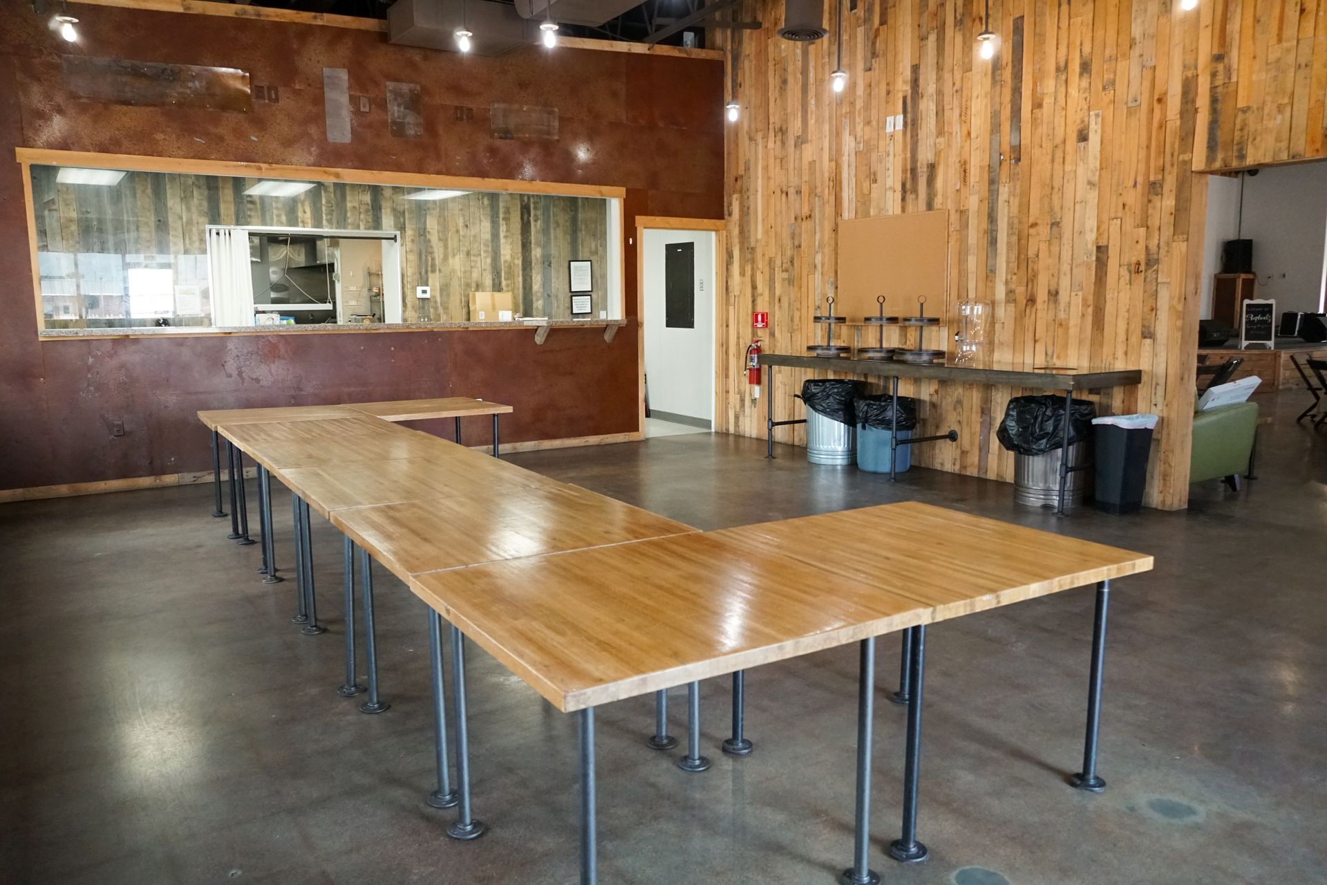 Long wooden table with metal legs in a large room with wood-paneled walls and a concrete floor.