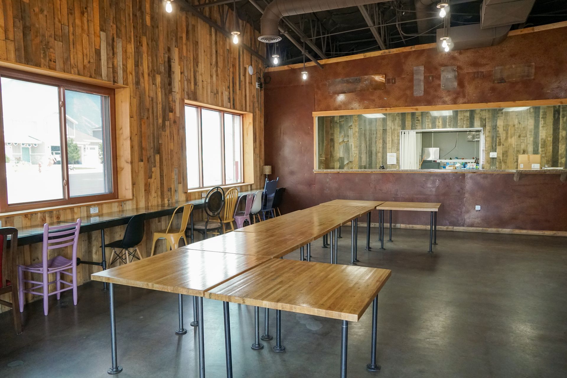 Interior of a rustic event space with wooden walls, long tables, and a view into a kitchen area.