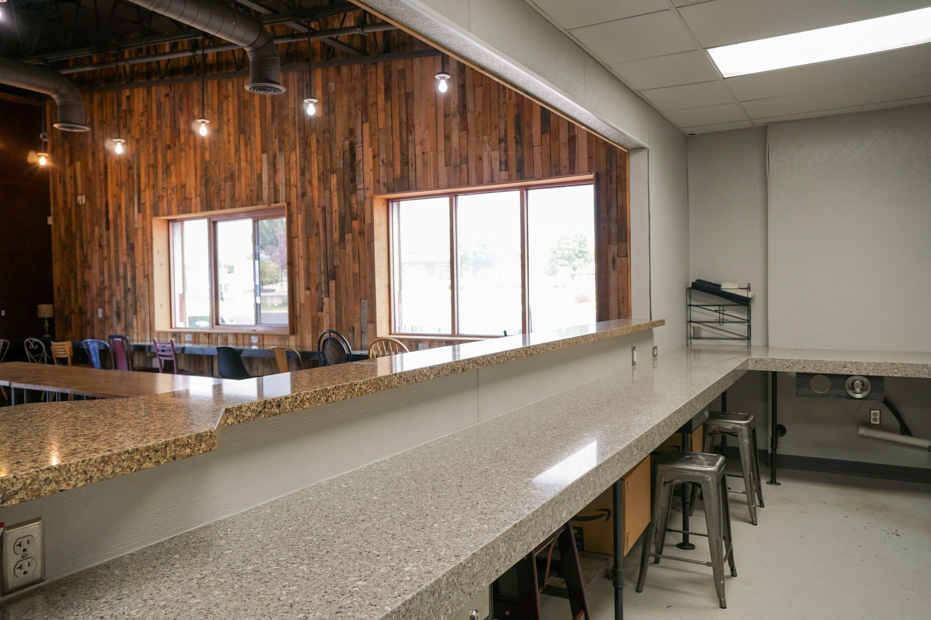 Long countertop with stools, leading to a window-lined wall with wooden paneling; interior space.