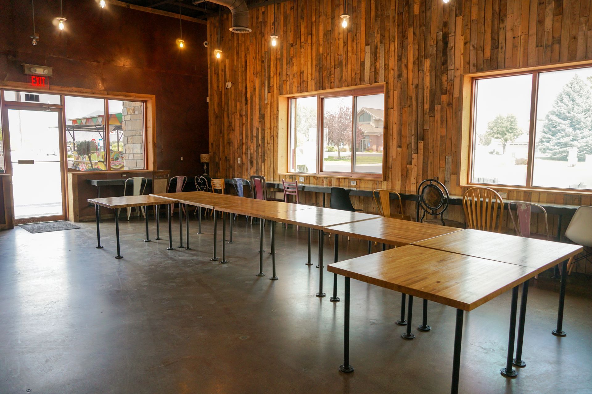 A U-shaped arrangement of tables in a room with wood-paneled walls and windows, ready for a gathering.