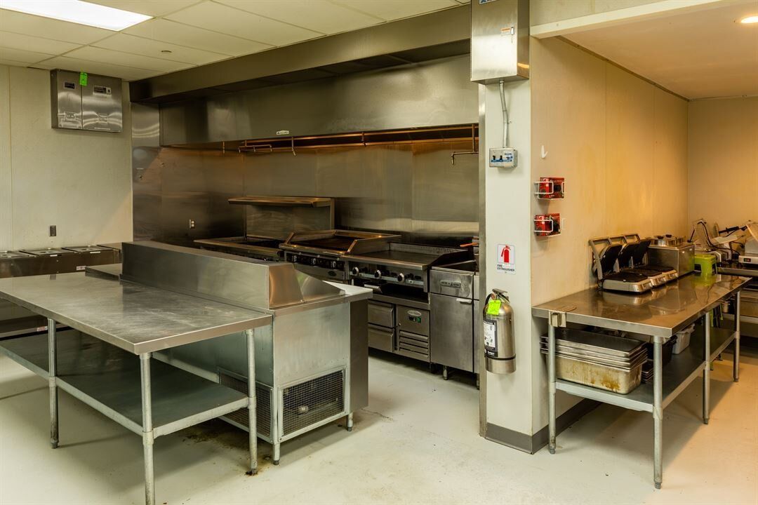 A large kitchen with stainless steel appliances and tables.