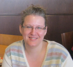 A woman wearing glasses and a striped sweater is smiling for the camera.