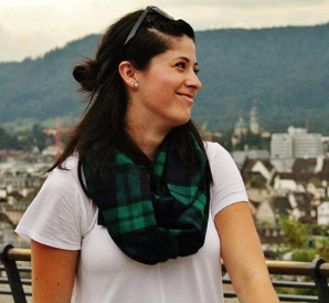 A woman wearing a white shirt and a green and black scarf is standing on a balcony.