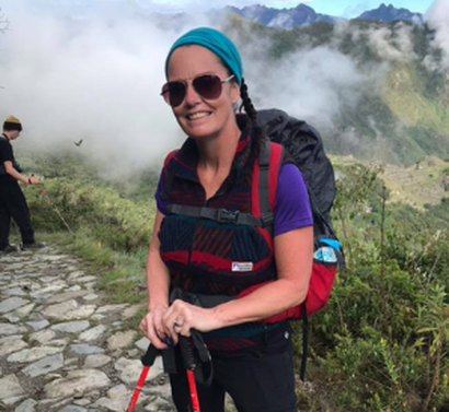 A woman wearing sunglasses and a backpack is hiking in the mountains.