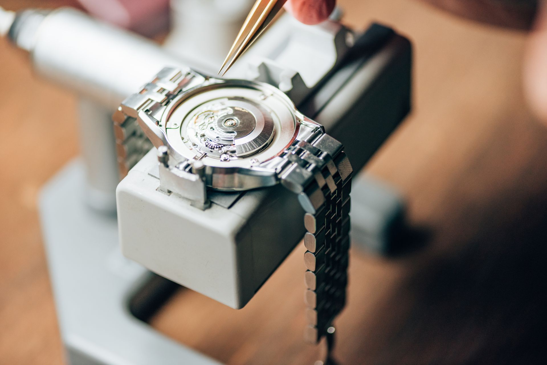Watch being repaired with tweezers, held in a watch repair tool.