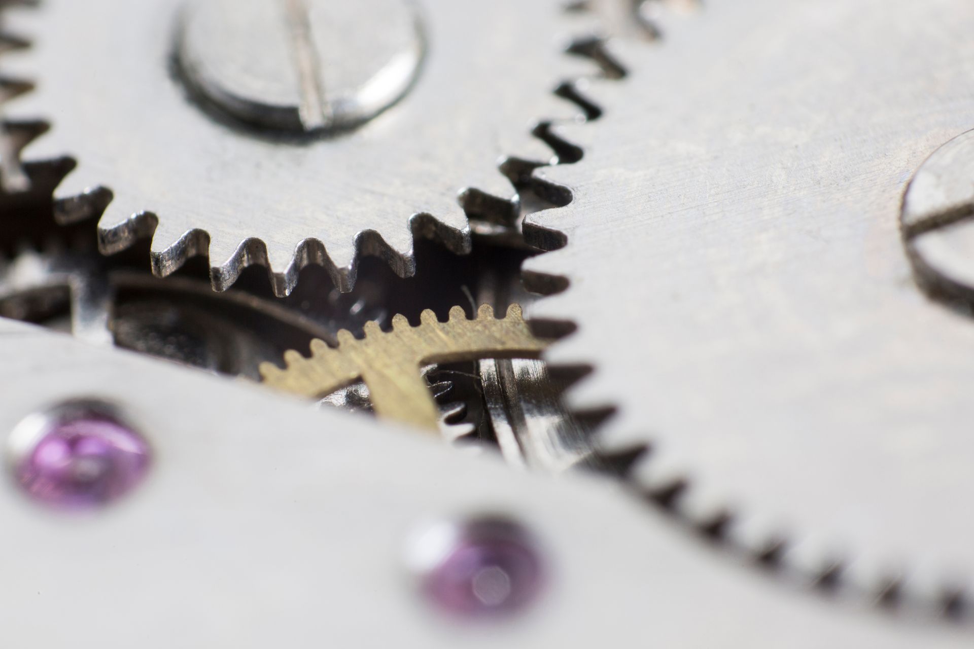 Close-up of clock gears meshing, silver and gold metal, purple jewel accents.