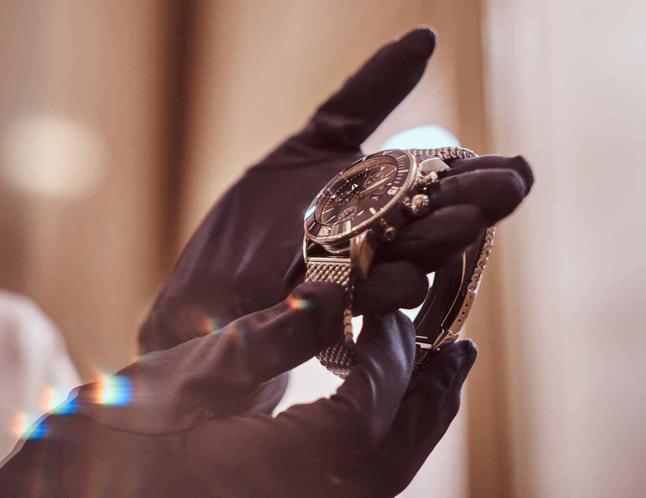 Gloved hands hold a shiny, gold wristwatch with a mesh band.