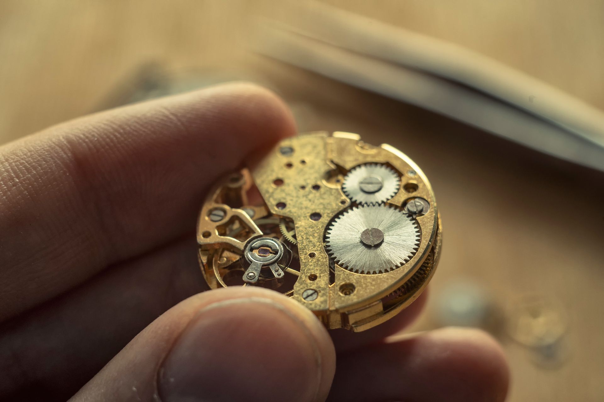 Hand holding a small, gold watch mechanism with visible gears and components; watch repair.