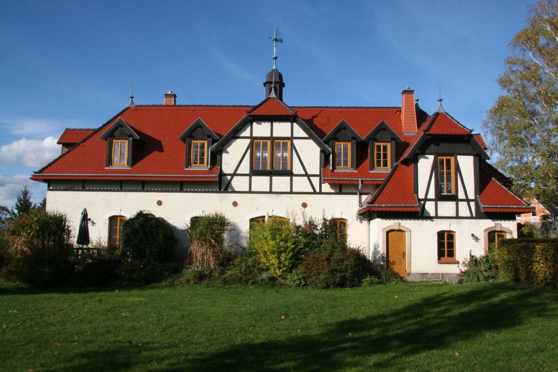 Zweistöckiges Gebäude mit rotem Ziegeldach und weißer Fassade mit schwarzen Zierelementen an einem sonnigen Tag.