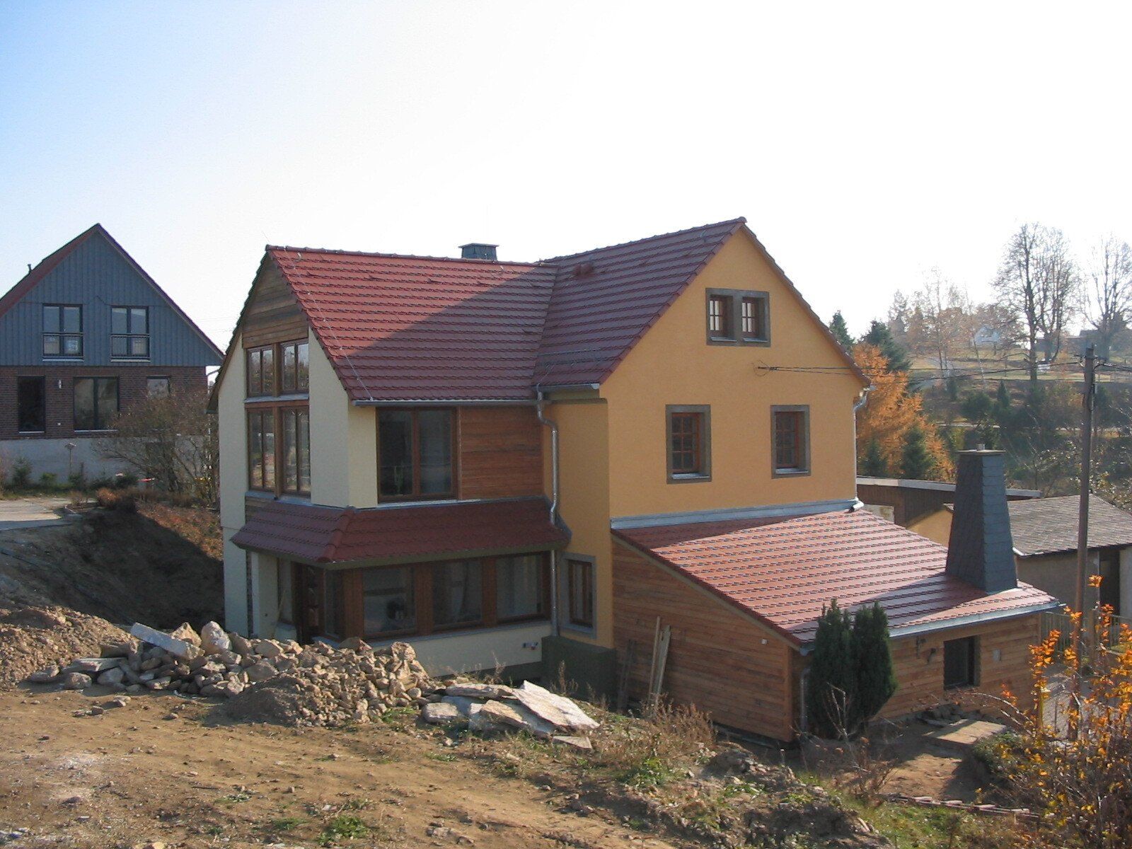 Ein Haus mit gelbem und rotem Dach am Hang mit Holzelementen und im Hintergrund ein weiteres Haus.