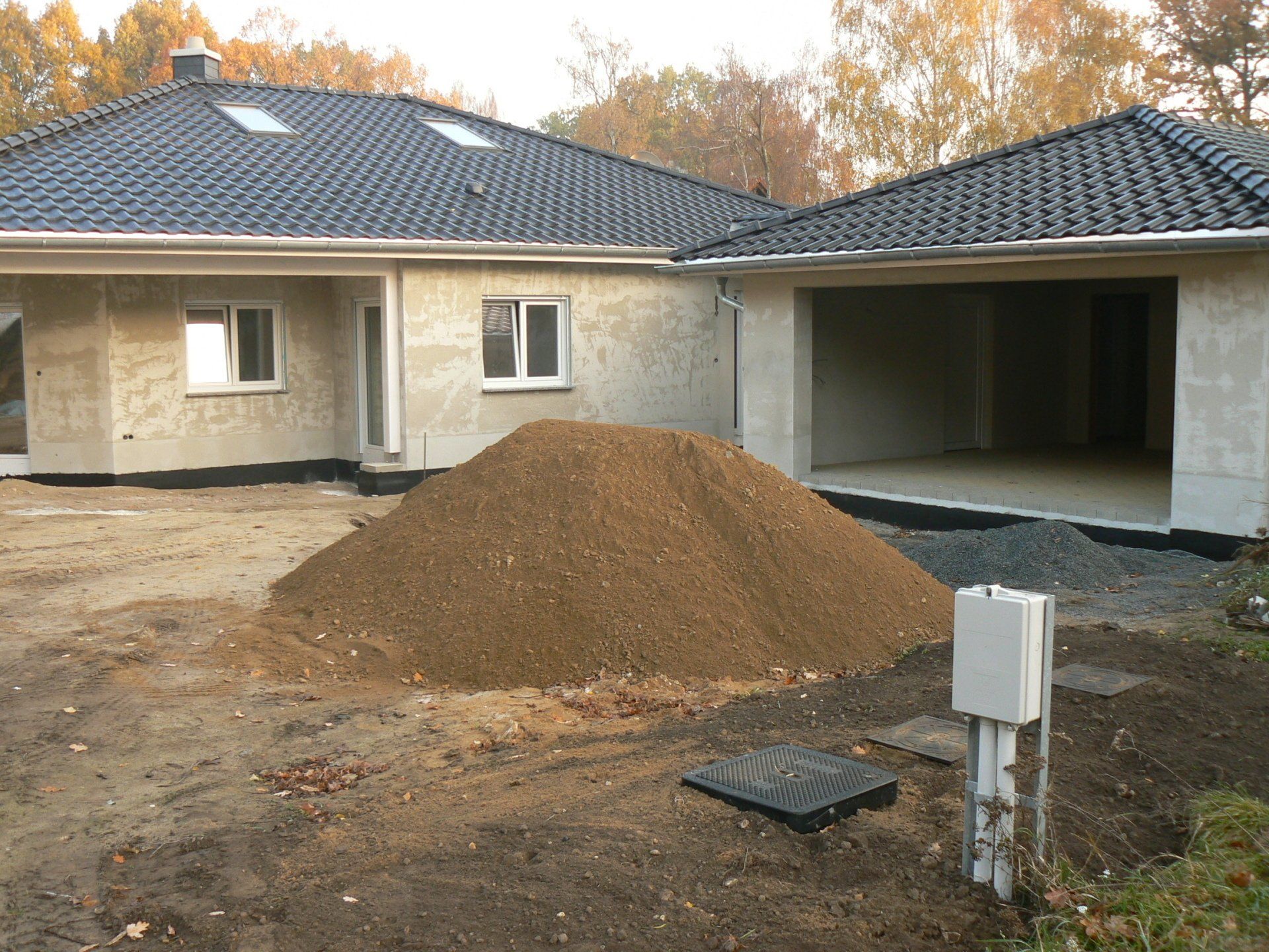 Ein großer Erdhaufen vor einem teilweise errichteten Haus mit offener Garage.