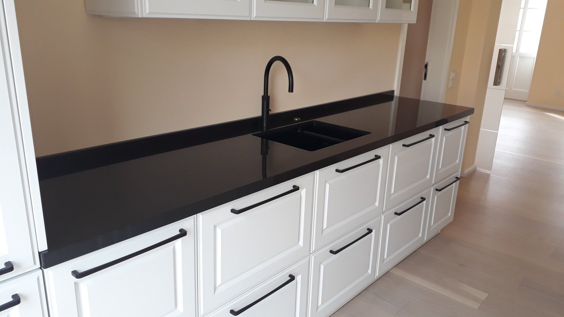 Weiße Küchenschränke mit schwarzer Arbeitsplatte und Armatur.