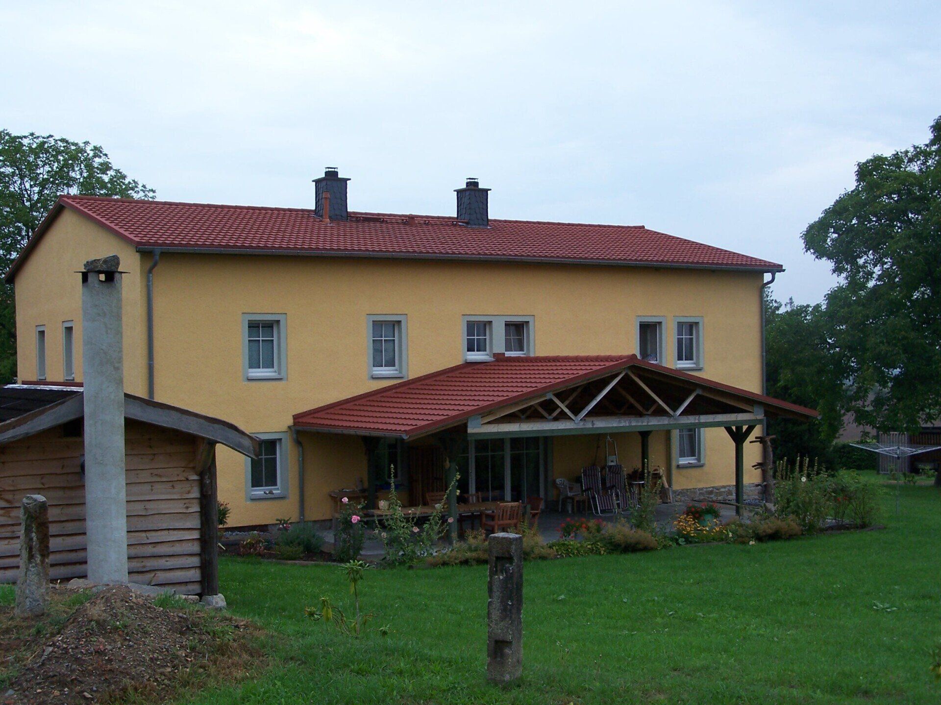 Gelbes zweistöckiges Haus mit rotem Dach und überdachter Veranda auf einem grünen Rasen.