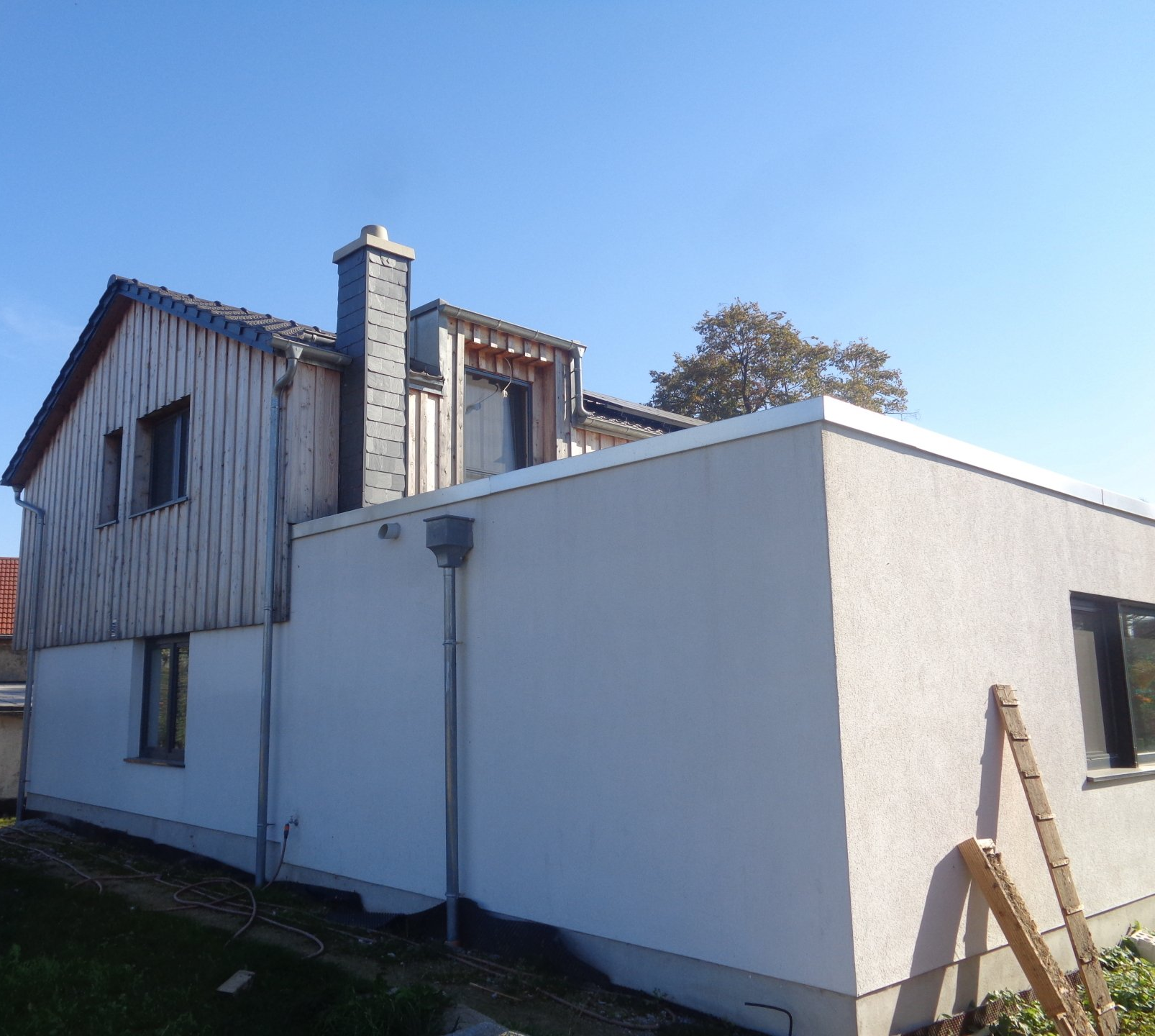 Zweistöckiges Haus mit Holzverkleidung und Stuckfassade, Schornstein und blauem Himmel.