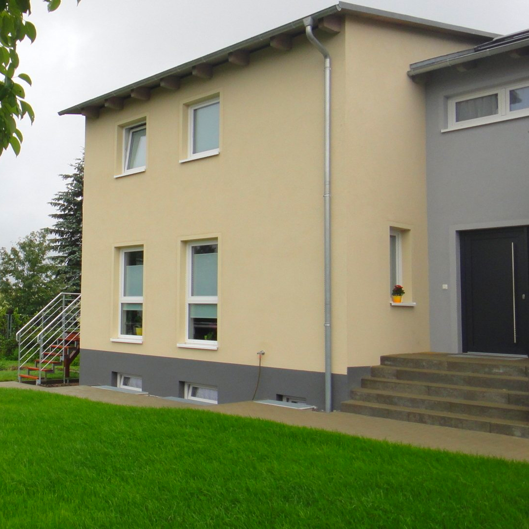 Zweistöckiges beigefarbenes Gebäude mit grauen Zierelementen. Rasenfläche davor.