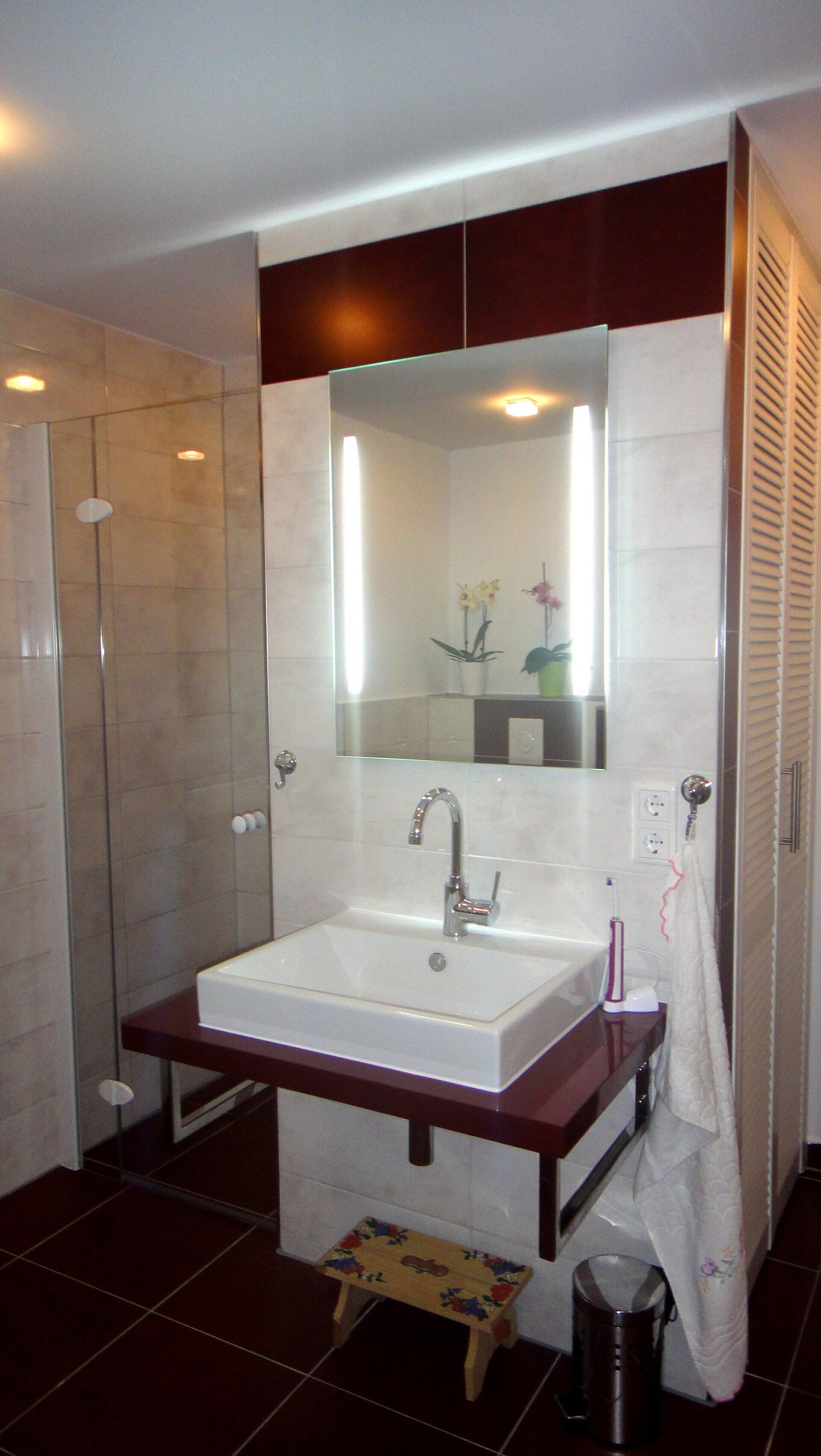 Badezimmer mit weißem, quadratischem Waschbecken auf bordeauxroter Arbeitsplatte, großem Spiegel und Duschkabine.