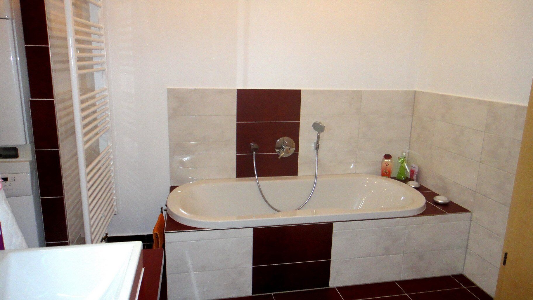 Badezimmer mit weißer Badewanne, bordeauxroten und cremefarbenen Fliesenakzenten und einem Handtuchhalter.