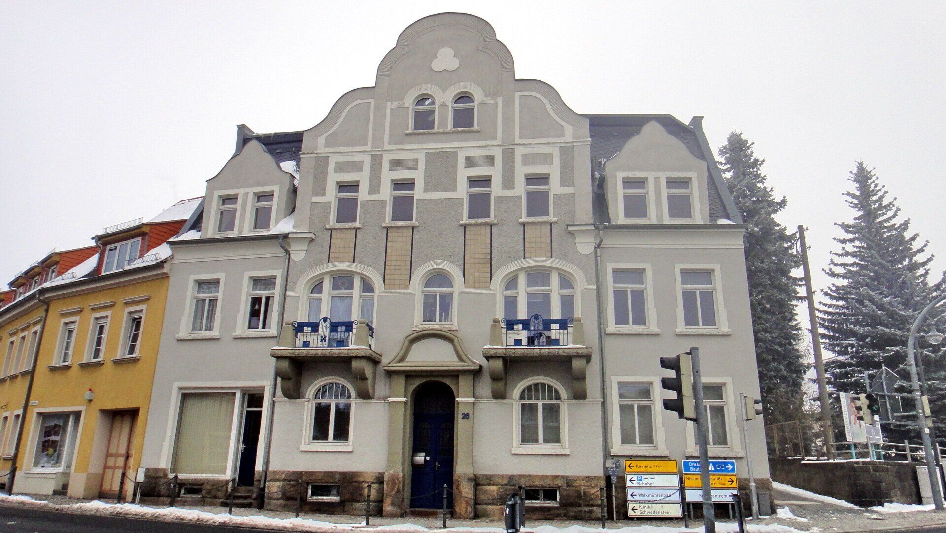 Grau-weißes mehrstöckiges Gebäude mit vielen Fenstern; Schnee auf dem Boden.