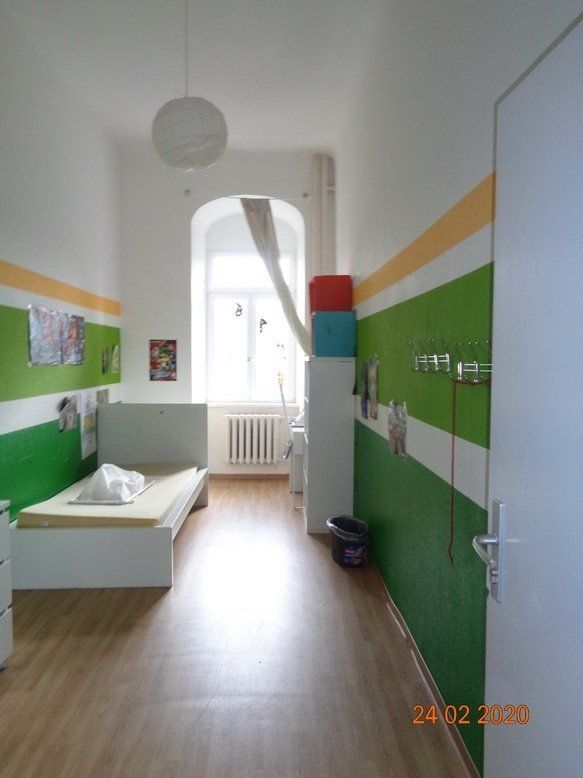 Schmale, farbenfrohe Krankenstation mit Bett, Fenster und Stauraum. Die Wände sind grün, weiß und gelb.