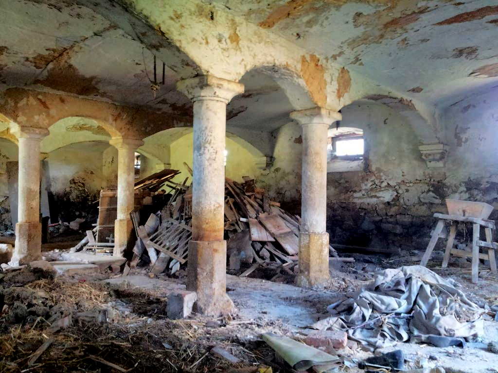 Verfallenes Interieur mit Steinsäulen und Schutt. Rissige Wände und gewölbte Decke.